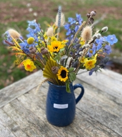 Florists choice of yellow and blue fresh and dried flowers in a heavy ceramic jug.